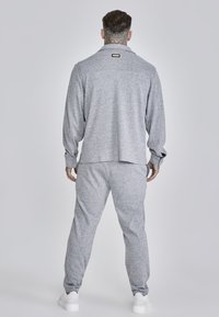 Set di abbigliamento lounge grigio con trama, composto da una maglia a maniche lunghe con colletto e pantaloni affusolati. Scarpe bianche completano il look. Nessun motivo prominente.