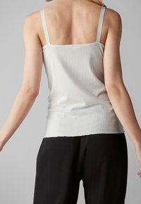 Camiseta de tirantes blanca con diseño acanalado y tirantes estrechos, que presenta un diseño ajustado y una textura suave. Se lleva combinada con pantalones negros.