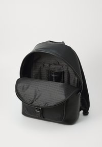 Un sac à dos noir en simili cuir texturé, avec une fermeture éclair, un intérieur ouvert avec une doublure à motif logo et une petite poche.