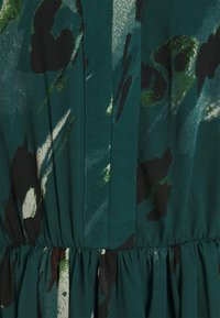 Grön tyg med abstrakta svarta och gröna mönster; har en resårmidja med veck, slät textur och subtil lyster.