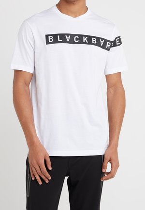 Homme portant un T-shirt blanc à manches courtes avec une bande horizontale noire traversant la poitrine et la manche, texte "BLACK BARRE" en lettres blanches.