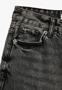 Vaqueros de denim negros con una textura ligeramente deslavada, que presentan un bolsillo frontal y herrajes de botón plateado a lo largo de la cintura.