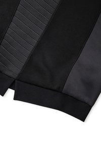 Schwarze Sportjacke mit strukturierten und glatten Stoffpaneelen, gerippten Bündchen und kontrastierenden satinähnlichen Akzenten an den Seiten.