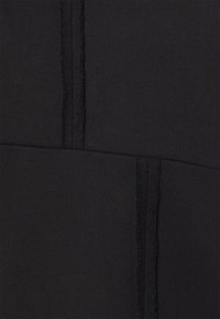 Il tessuto nero presenta una superficie testurizzata con cuciture e pannelli visibili, creando un design strutturato con sottili variazioni di texture.