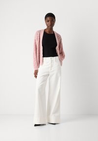 Cardigan rosa a maglia sopra una canotta nera, abbinato a pantaloni bianchi a gamba larga. Scarpe con tacco nere completano l'outfit. Texture morbide e colori chiari.