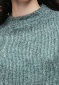 Groene geribbelde gebreide trui met een hoge hals en een zachte textuur, met verschillende tinten groen voor een subtiel patroon.