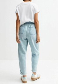 Celana jeans denim biru muda dengan pinggang elastis, cuff yang dilipat, dan dua kantong belakang, dipadukan dengan kemeja lengan pendek putih dan sepatu sneakers.