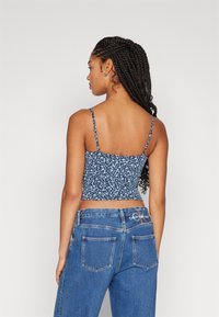 Top cropped azul floral com alças finas, feito de tecido leve. Usado com jeans de denim azul de cintura alta com bolsos traseiros.