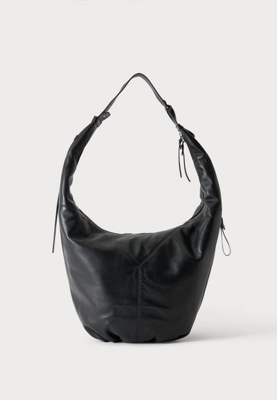 Sac à bandoulière en cuir noir souple, doté d’une longue bandoulière, d’une couture centrale et d’une fermeture zippée, sur fond clair.