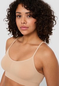 Beige bralette med tunna band, slät textur och sömlös design. Har en rundad form och subtila sömnadsdetaljer.