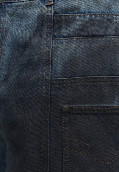 Κοντινό πλάνο σκούρων μπλε τζιν με πίσω τσέπες και λεπτομερείς πορτοκαλί ραφές.