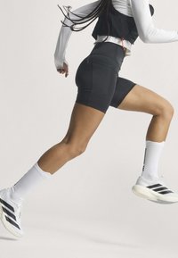 Personne portant un short de cyclisme noir, un haut blanc à manches longues, des chaussettes blanches, courant à mi-rythme sur un fond uni.