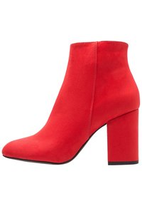 Czerwone zamszowe botki za kostkę z długim noskiem i masywnym obcasem. Charakteryzują się bezszwową konstrukcją i gładką fakturą.