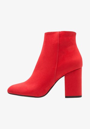 Czerwone zamszowe botki za kostkę z długim noskiem i masywnym obcasem. Charakteryzują się bezszwową konstrukcją i gładką fakturą.