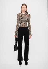 Transparente Langarmbluse mit Hahnentritt-Muster, kombiniert mit schwarzen Schlaghosen. Die Accessoires umfassen eine schwarze Tasche und spitze Absatzschuhe.