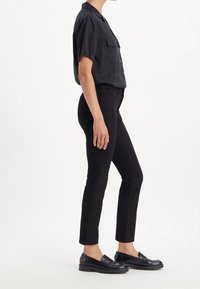 Camisa negra de botones y manga corta, combinada con jeans negros ajustados y mocasines negros. Diseño simple y estilizado sin patrones visibles.