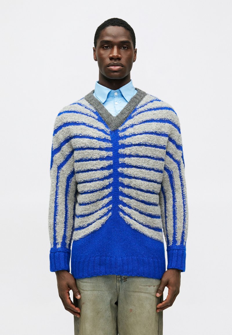 Sweater de punto azul y gris con escote en V, que presenta patrones acanalados y rayas en contraste, acabado texturizado y corte holgado.