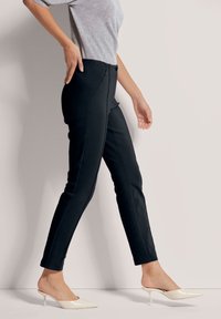 Zwarte aansluitende broek met voornaaddetails, gecombineerd met puntige instapschoenen. Het materiaal lijkt glad met een verzorgde uitstraling.