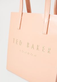 Rosa syntetisk lær tote bag med preget "TED BAKER LONDON"-tekst i gull. Har to flate håndtak og en glatt tekstur.