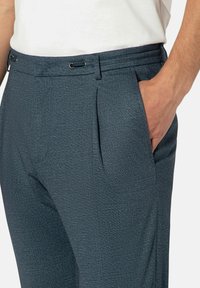 Op maat gemaakte broek van donkerblauw textuurstof met plooien. Beschikt over een elastische tailleband met trekkoord en zijzakken. Gladde, gestructureerde ontwerp.