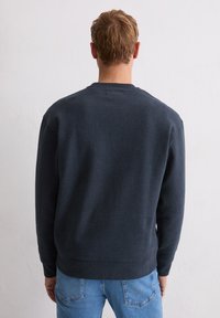 Granatowa bluza z okrągłym dekoltem i szczegółami ściągaczy na rękawach. Tkanina wydaje się miękka o lekkiej teksturze, dopasowana w talii.