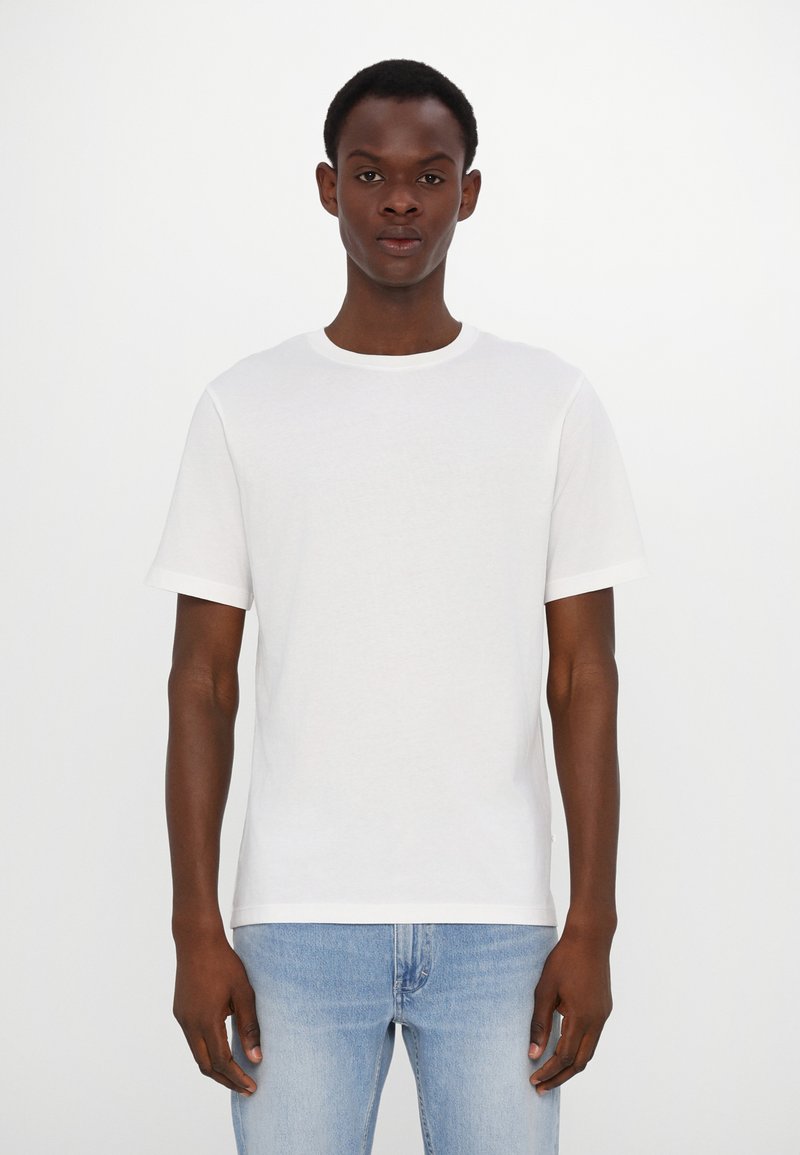 White cotton t-shirt with short sleeves, crew neck, and a straight fit. Worn with light blue denim jeans. No visible patterns or accents.