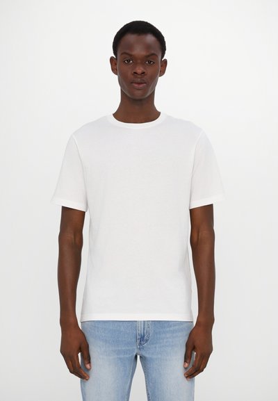 Weißes Baumwoll-T-Shirt mit rundem Ausschnitt und kurzen Ärmeln, zeichnet sich durch eine glatte Textur aus. Wird mit hellblauen Denim-Jeans getragen.