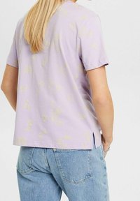 Fialové tričko s krátkým rukávem a zlatým květinovým vzorem, vyrobené z měkké bavlny, rovného střihu a se bočními rozparky na spodním lemu pro snadný pohyb.