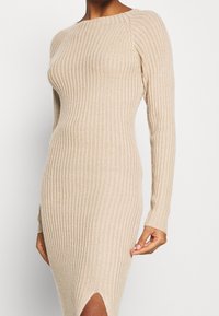 Robe beige côtelée avec manches longues, col rond et fente latérale. Confectionnée en tissu tricoté texturé, elle épouse étroitement la silhouette.