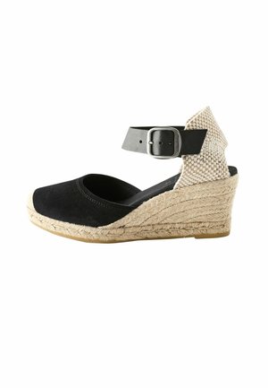 Espadrille compensée noire avec talon tissé beige, plateforme enveloppée de jute et bride de cheville noire avec boucle argentée.