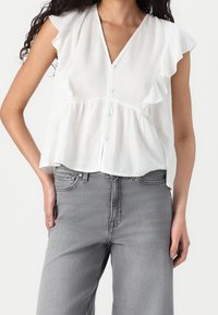 Witte blouse met korte mouwen, voorzien van een ruffles trim, V-hals, knoopsluiting en een losse fit, gecombineerd met lichtgrijze wijde jeans.