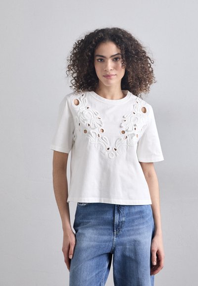 White cotton t-shirt featuring intricate floral embroidery with cut-out details around the neckline and sleeves. Loose fit, short sleeves.