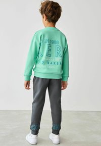 Mintgrön sweatshirt med stor blå text, tillsammans med mörkgrå joggers med blå detaljer. Vita sneakers fulländar outfiten.