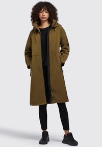 Parka impermeabile verde oliva con cerniera nera, tasche laterali e cappuccio. Presenta un design lungo e una texture liscia e opaca.
