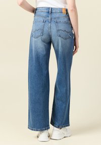 Szerokie niebieskie dżinsy z wysokim stanem, tylnymi kieszeniami z falowanym wzorem stębnowania oraz surowym dołem wykończonym na kostkach.