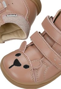 Deux chaussures roses pour tout-petits avec une broderie de visage d’ours sur les orteils et des sangles Velcro réglables sur le dessus.