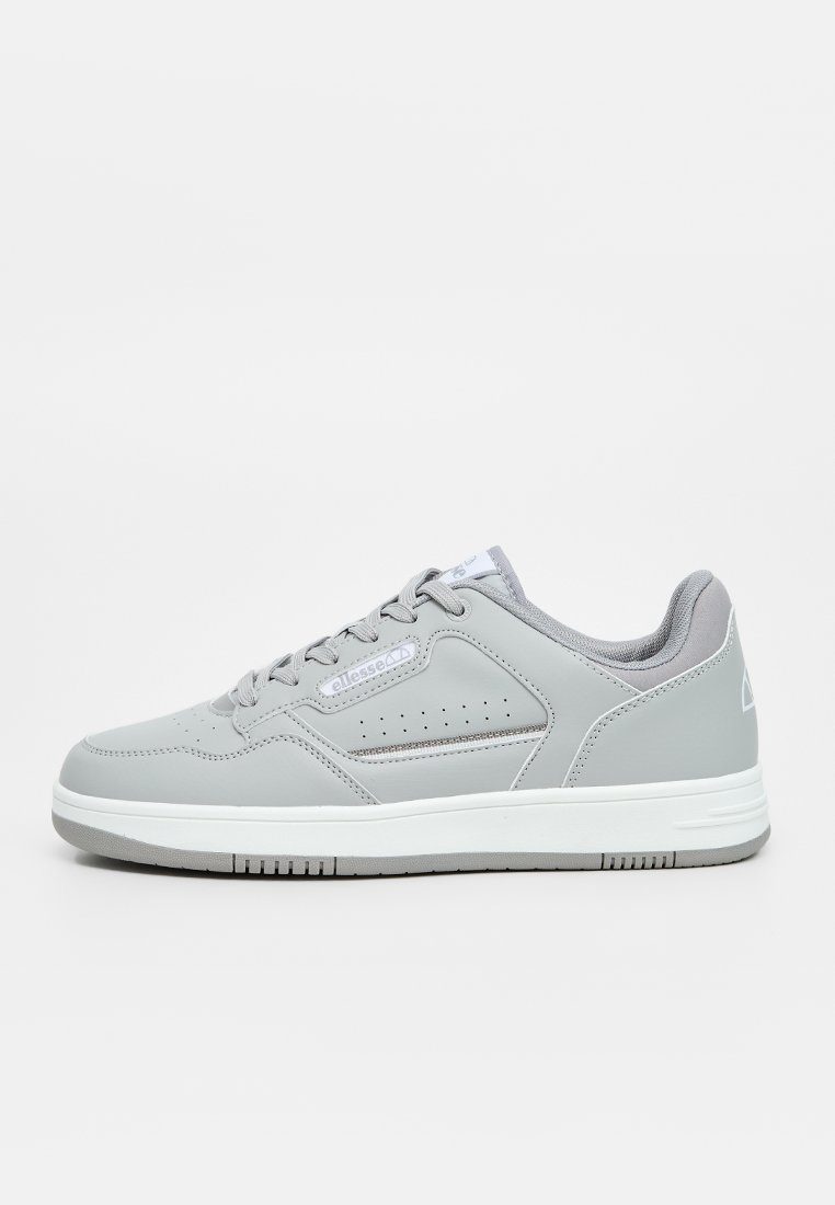 Zapatilla atlética gris con material sintético, punta redondeada, detalles perforados en los lados, suela blanca plana y acentos en gris claro.
