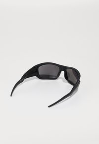 Ochelari de soare negri cu un finisaj mat, design înconjurător și lentile întunecate. Dispune de brațe subțiri cu o branding subtil aproape de balamale.