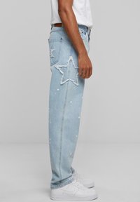 Light blue denim jeans with a distressed star design on the thigh and paint splatter accents. Finished with a standard waistband and pockets.