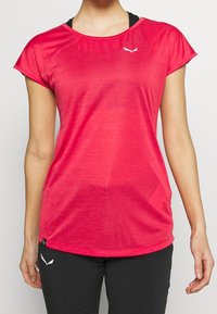 Camiseta deportiva fucsia de manga corta, con escote redondo y tejido ligero. Presenta un pequeño logo blanco en la parte delantera.