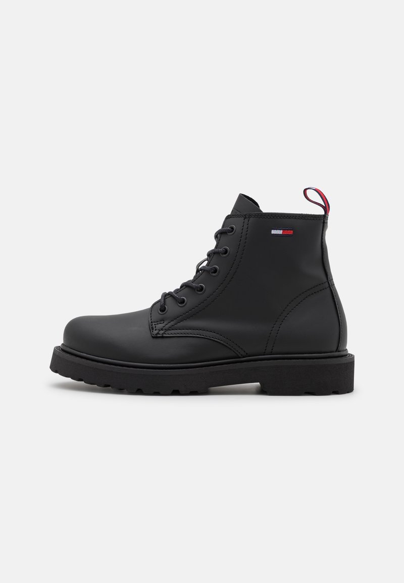 Bottine noire en cuir à lacets avec semelle épaisse et petit logo de la marque rouge, blanc et bleu sur le côté.
