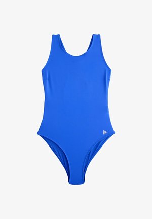 Femeie purtând un costum de baie albastru cu spatele decupat în formă ovală, văzută din spate, pe un fundal exterior neclar.