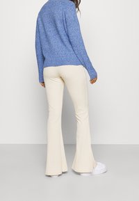 Pull en tricot bleu avec une coupe décontractée et un ourlet côtelé, associé à un pantalon évasé crème en tissu texturé et avec des fentes latérales.