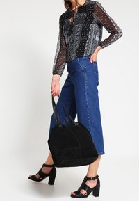Bolso de ante negro con doble correa, forma redonda y detalles de costura sutiles. Combinado con unos jeans de tiro alto azul y sandalias negras de tacón.
