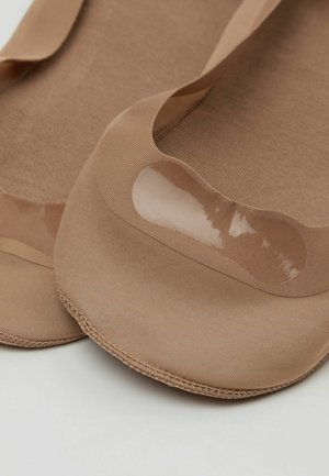 Béžové ponožky typu no-show s průhledným silikonovým proužkem na patě pro lepší uchopení, položeny na světlém povrchu.