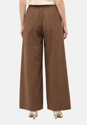 Femme portant un pantalon marron taille haute à jambes larges avec une ceinture élastique, debout, vue de dos, assorti à des talons beiges.