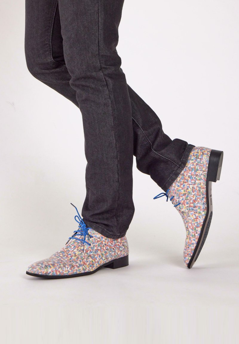 Patterned dress shoes in multicolored woven textile with blue laces, contrasted against dark denim jeans, showcasing a rounded toe and flat heel.