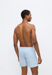 Φωτεινά γαλάζια βαμβακερά σορτς με ελαστική μέση, εμφανιζόμενα από πίσω. Λεπτή υφή, μήκος έως το γόνατο, μίνιμαλ σχεδιασμός.