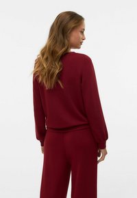 Felpa borgogna e pantaloni abbinati realizzati in tessuto morbido, con una vestibilità comoda, polsini a costine e un semplice scollo a girocollo.