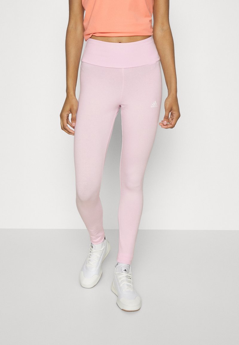 Leggings rosa chiaro realizzati in tessuto elasticizzato con una vita alta, con un piccolo logo bianco sulla coscia, abbinati a sneaker bianche.